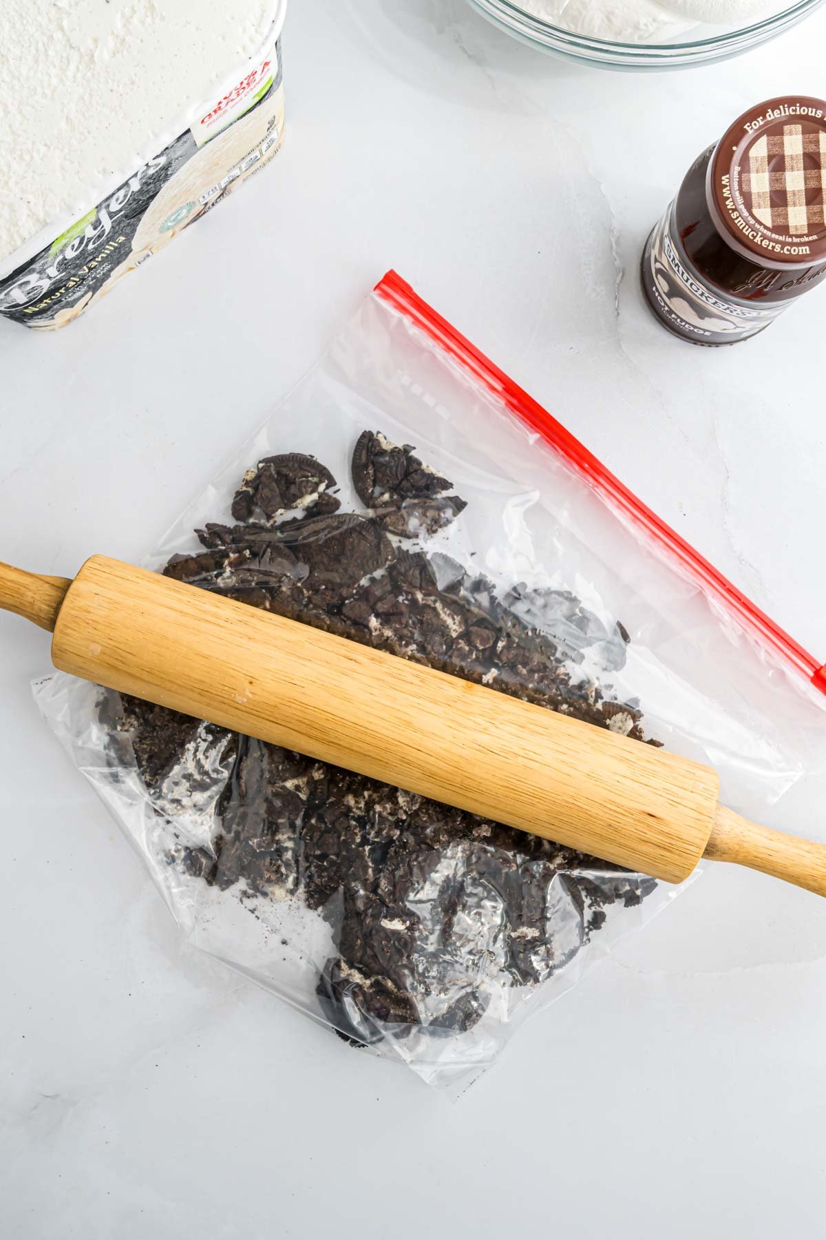 Oreo cookies in a resealable food storage bag being crushed by a rolling pin.