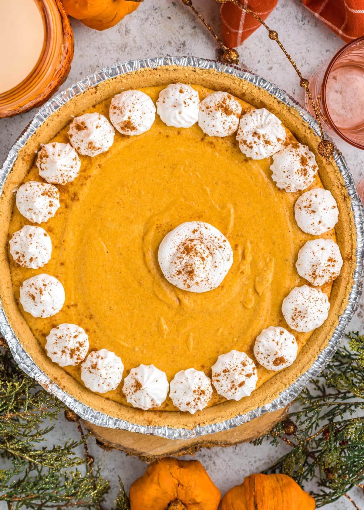 A pumpkin pie topped with dollops of whipped cream and sprinkled with cinnamon.