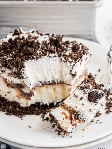 A piece of Oreo Ice Cream Cake on a plate with a fork loaded with a bite on it.