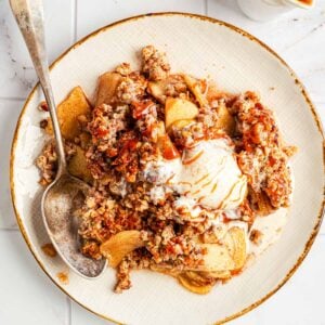 A plate of warm apple crisp with a scoop of vanilla ice cream on top.