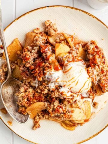 A plate of warm apple crisp with a scoop of vanilla ice cream on top.
