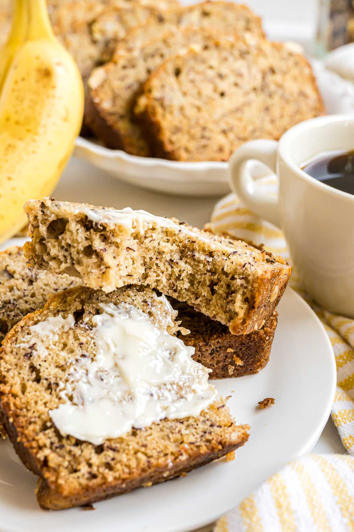 Sliced banana nut bread topped with softened butter on a small serving plate.