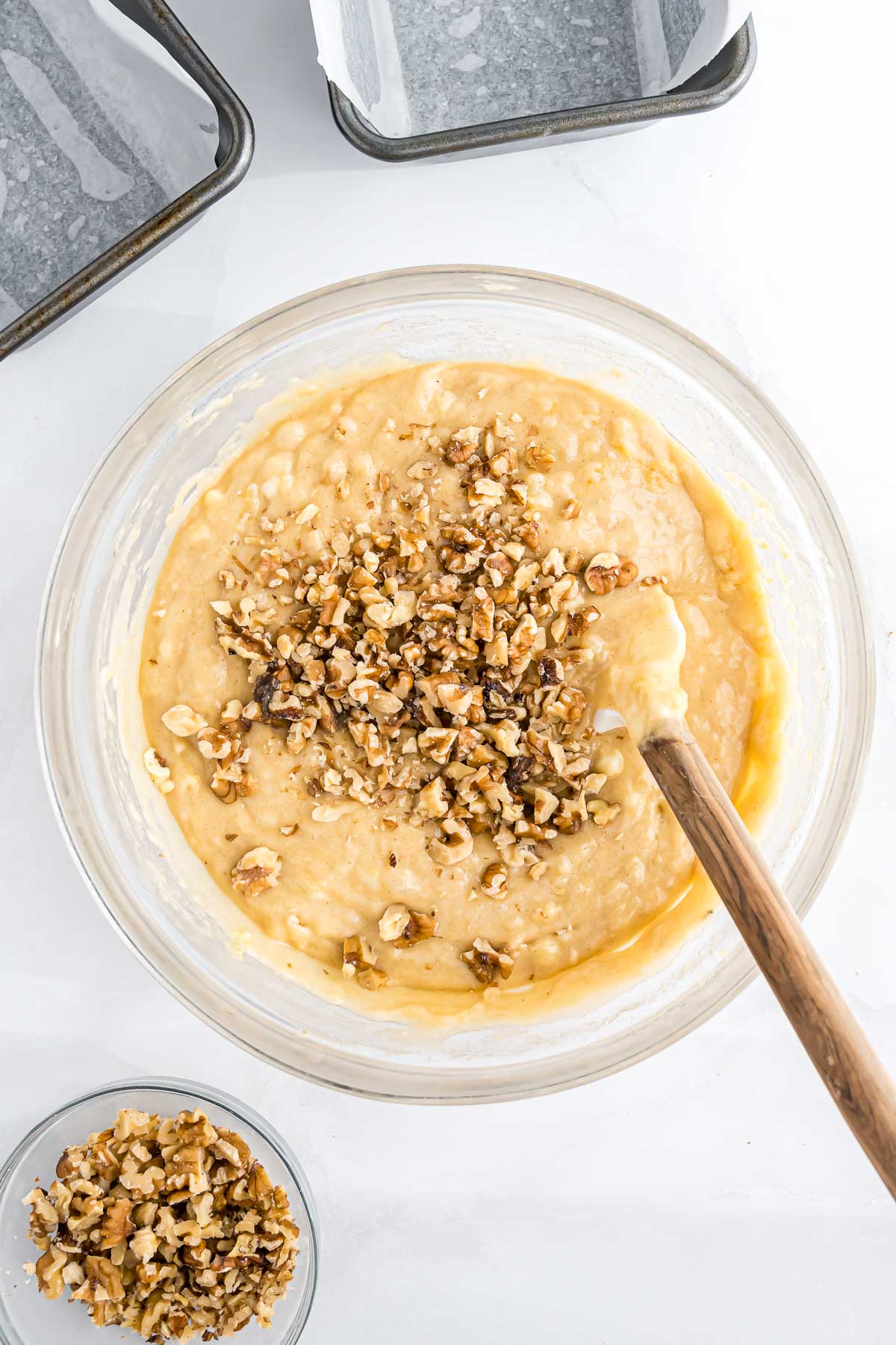 Chopped walnuts being added to the  banana nut bread batter in a large mixing bowl.
