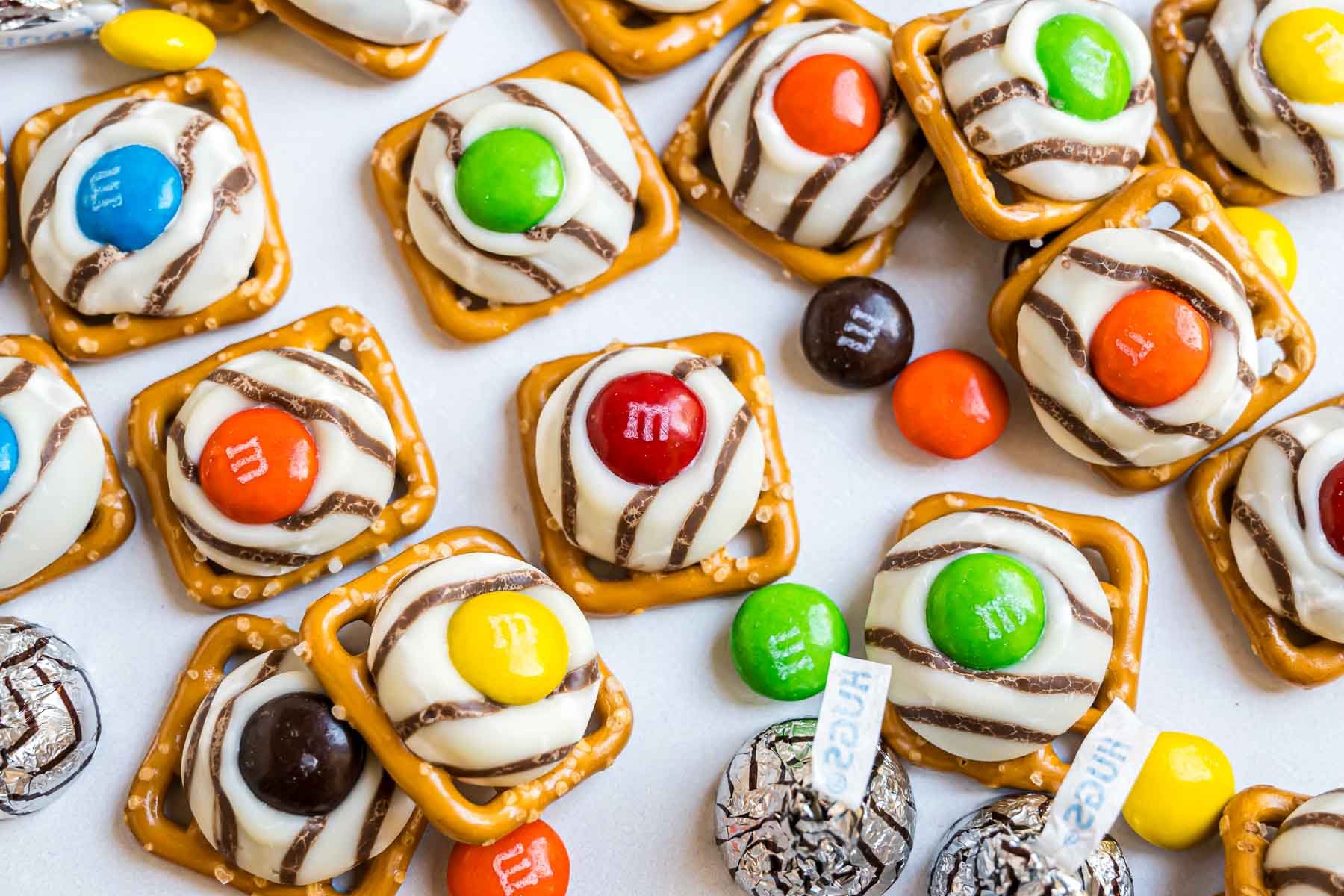Pretzel hugs on a piece of parchment with M&M candies and Hershey's Hugs scattered around them.