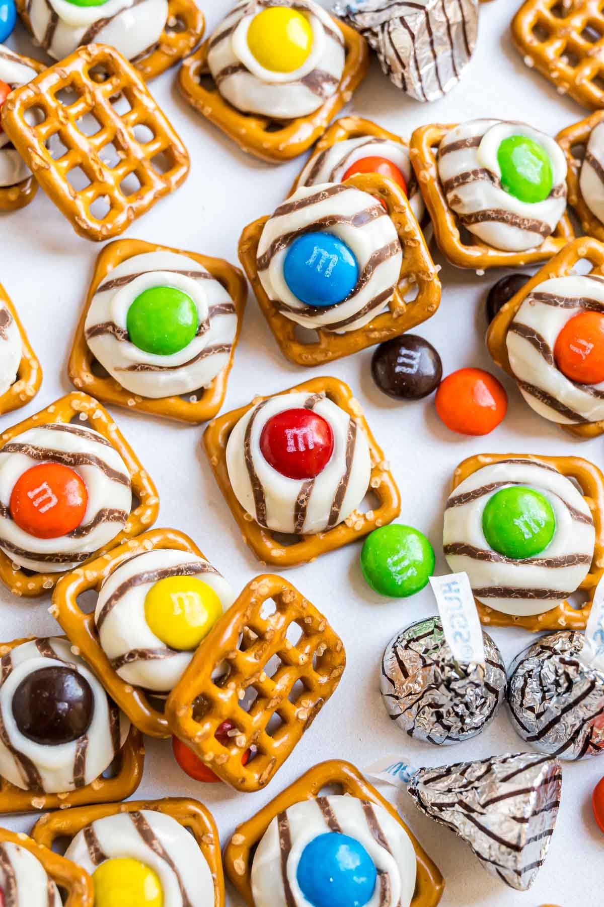Pretzel Hugs decorated with original M&M candies spread out on a piece of parchment paper.