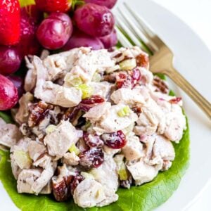 A serving of chicken pecan salad on a lettuce leaf with some fruit as a side.