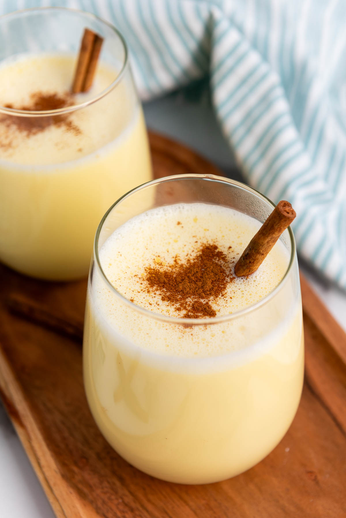 A glass of rich and creamy homemade eggnog garnished with ground cinnamon and cinnamon sticks.