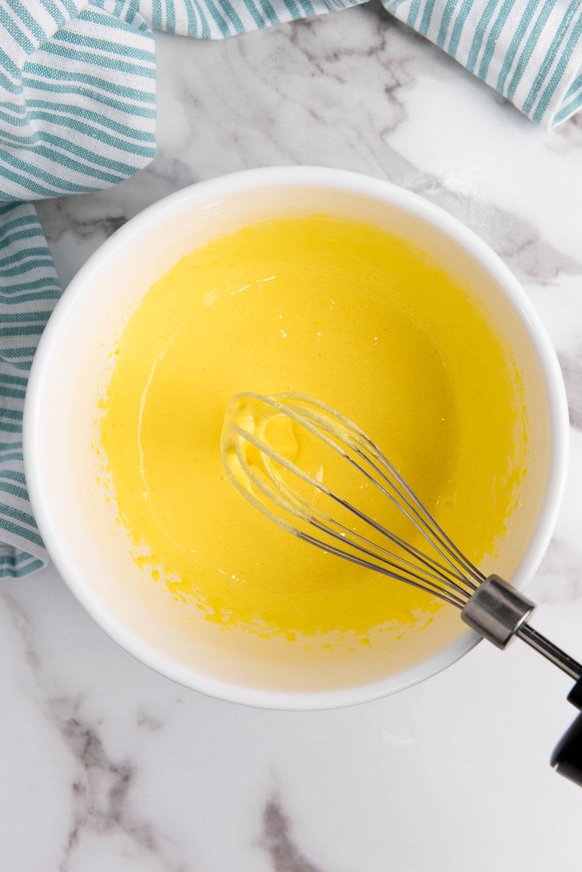 The egg yolks and granulated sugar being whisked together in a large mixing bowl.