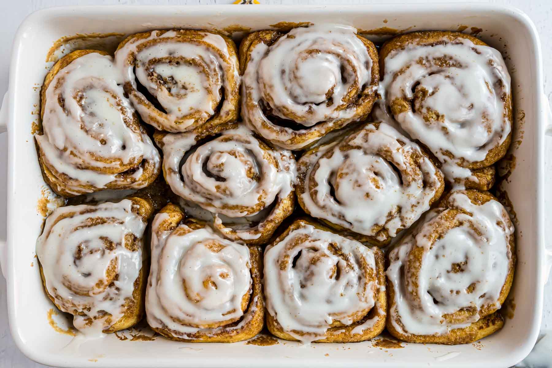 The baked cinnamon rolls in a dish with cream cheese frosting on top.