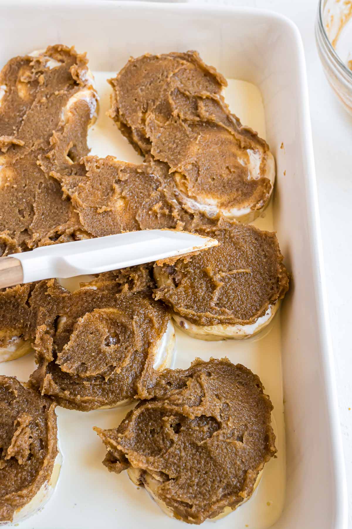 The butter mixture being spread on the tops of the cinnamon rolls before baking.