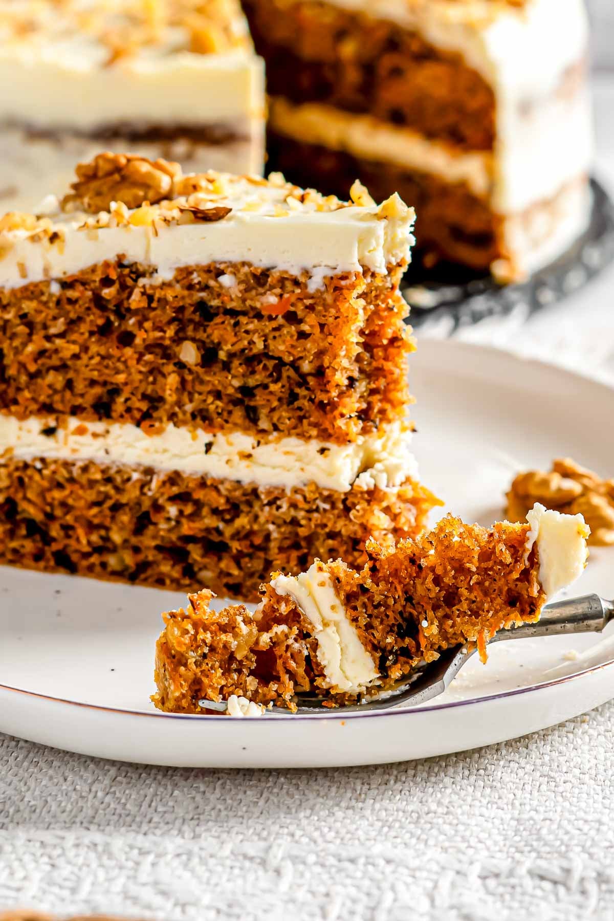 A bite of carrot cake on a fork resting on the side of a plate.