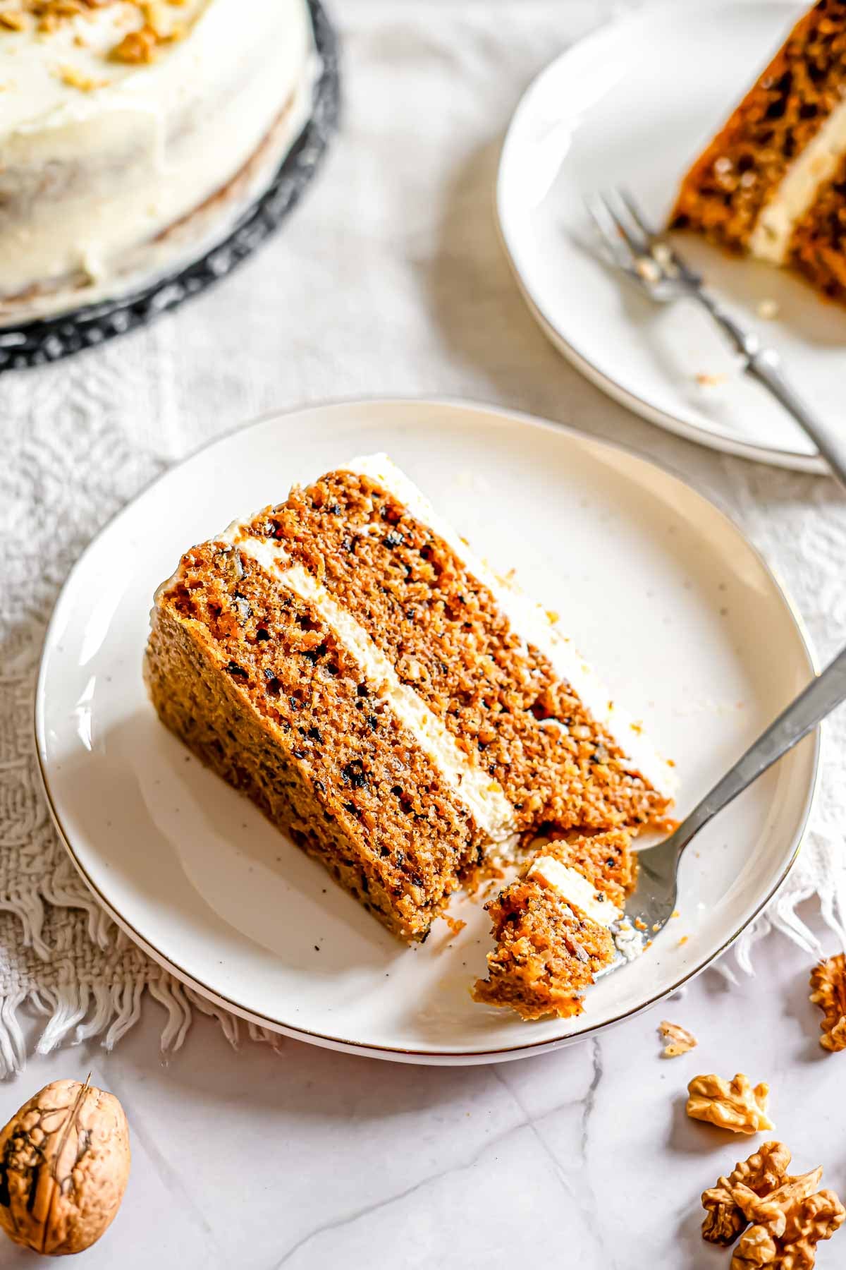 A piece of carrot cake with bite of carrot cake on a fork resting on the side of a plate.