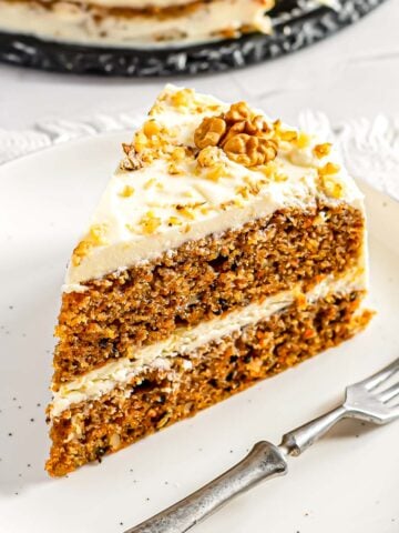 A piece of a double layered carrot cake with cream cheese frosting on a small serving plate.