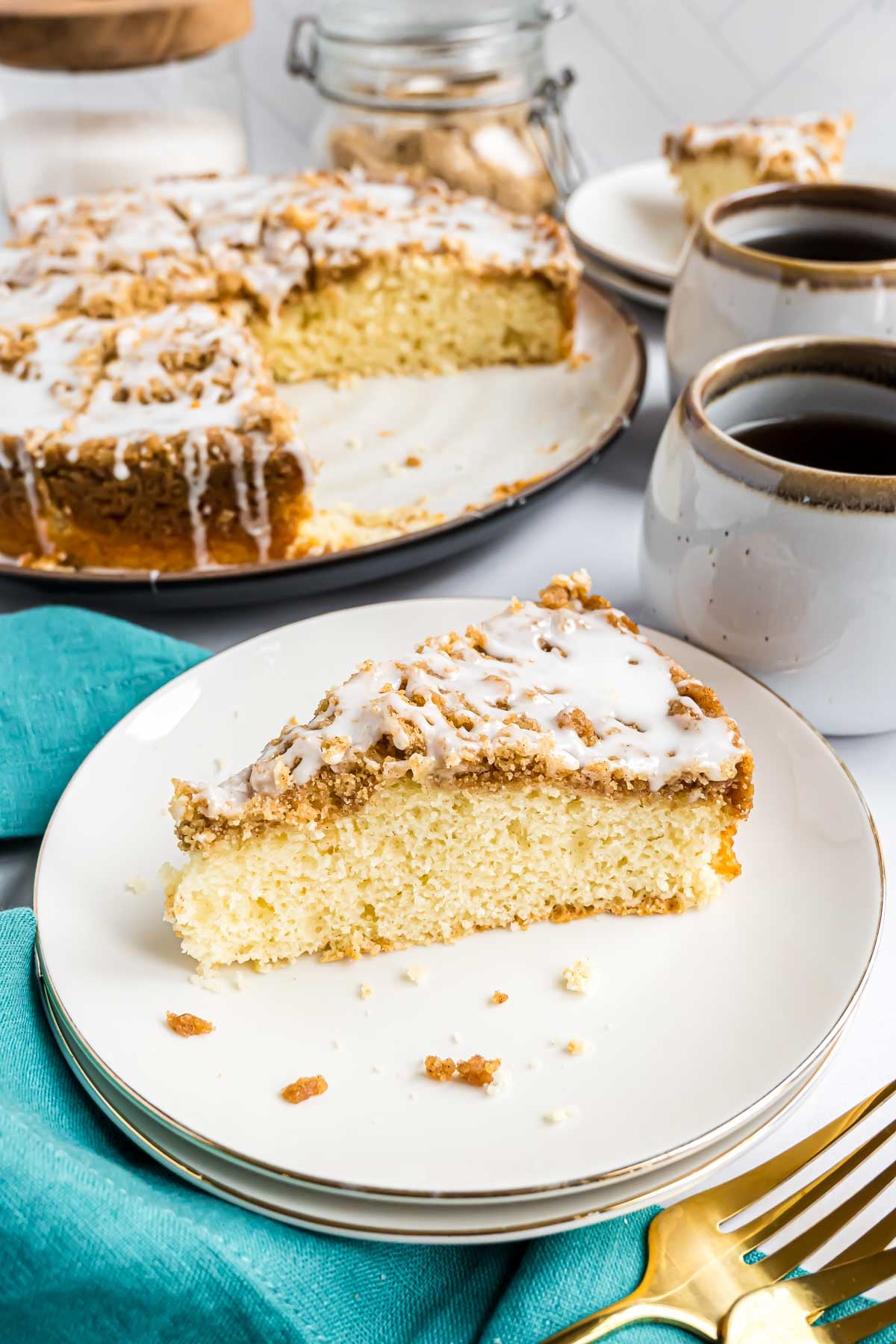 A piece of cinnamon streusel coffee cake on a serving plate. The full coffee cake can be seen in the background.