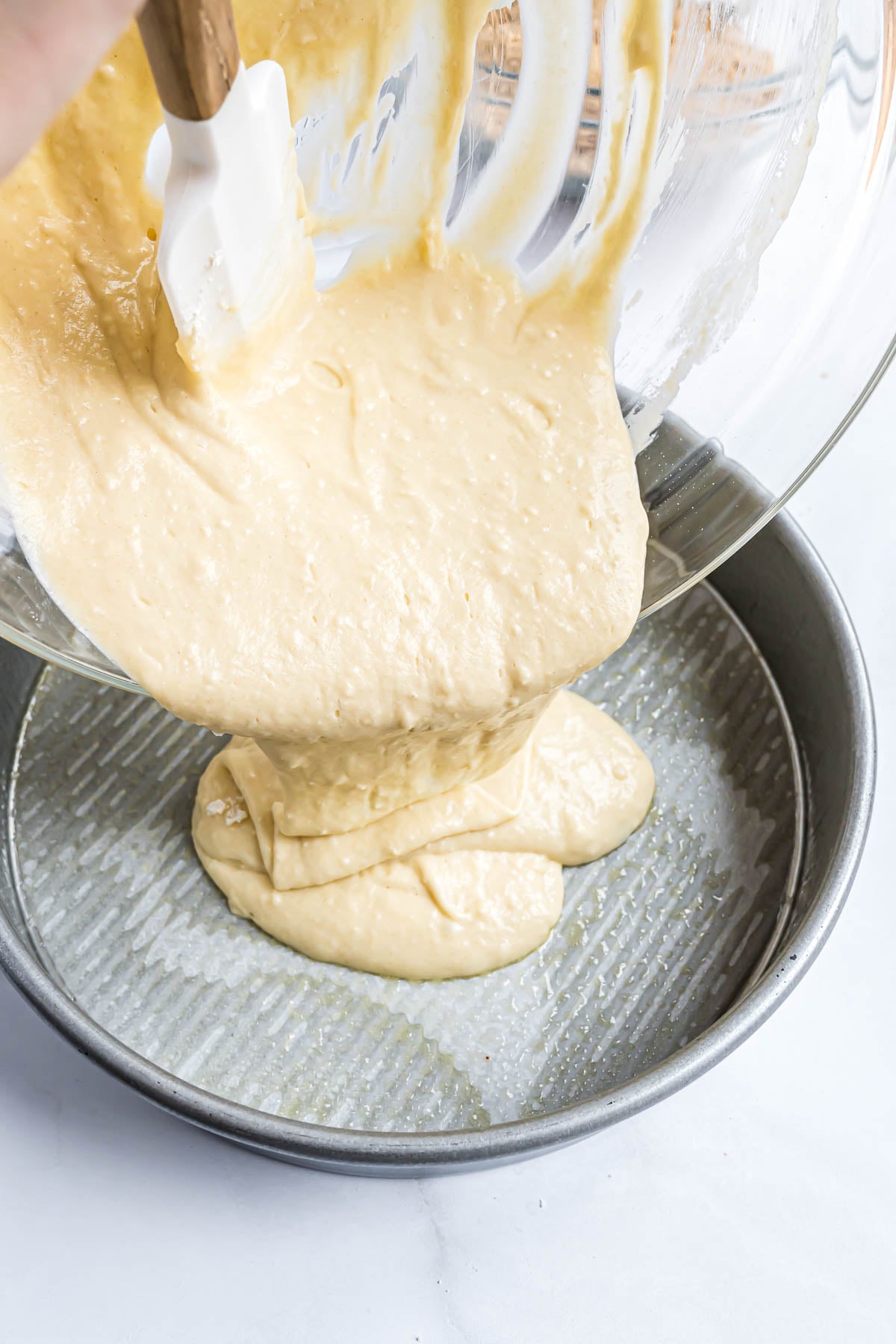 The coffee cake batter being poured into a round pan showing the thickness and texture of how the batter should look when mixed.