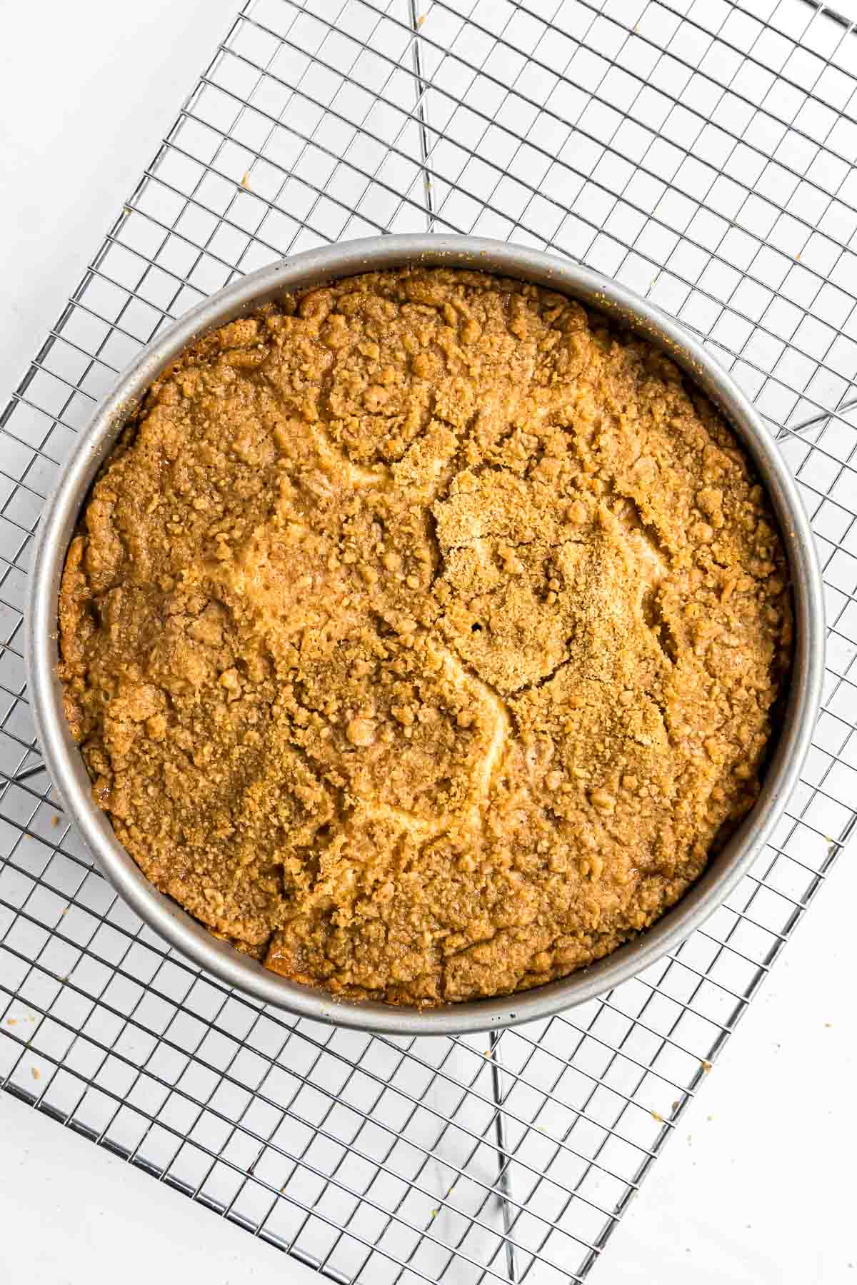 The coffee cake just as it comes out of the oven with a golden brown, domed top. It's sitting on a wire cooling rack.