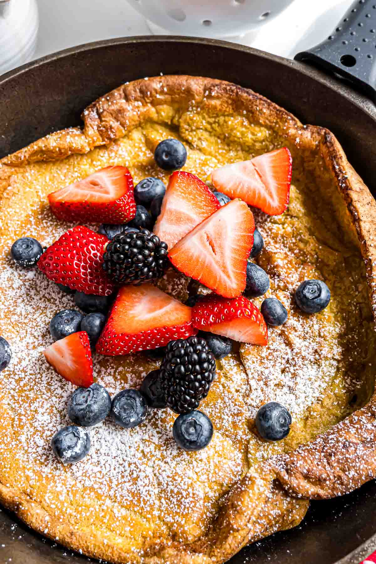 A baked German Pancake, topped with powdered sugar and berries, in a cast iron skillet