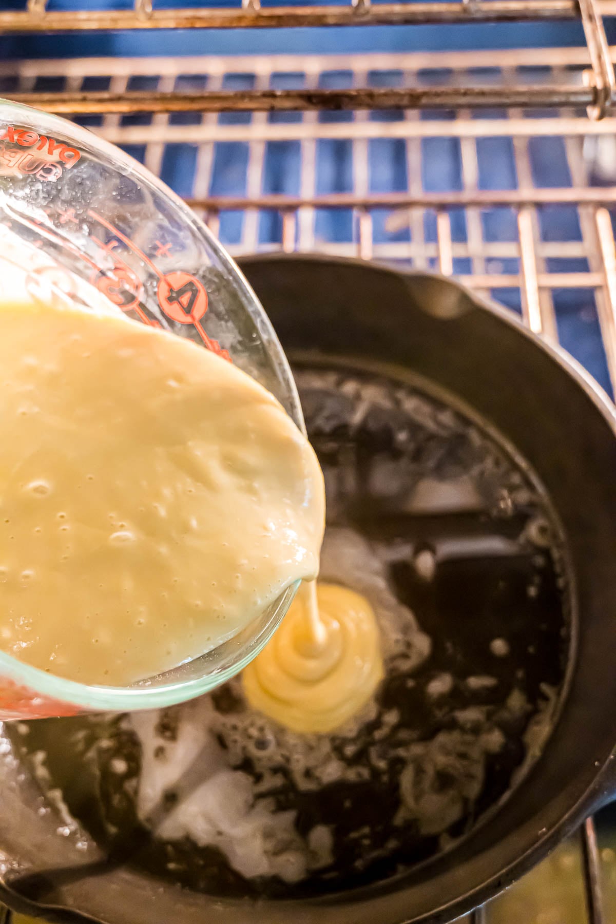 Pouring the batter from a large, glass measuring cup directly into the skillet sitting on the rack in the oven.