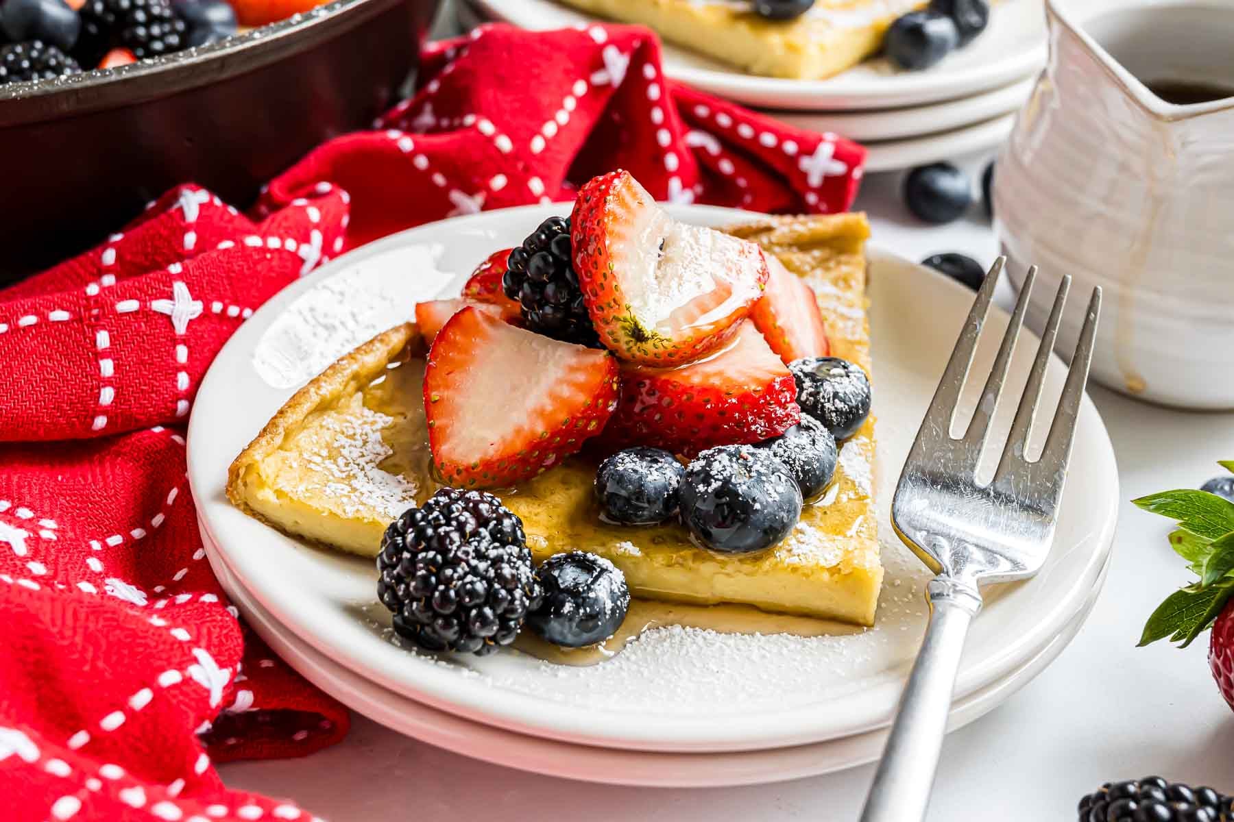 A piece of German pancake, topped with berries and powdered sugar, on a small serving plate.