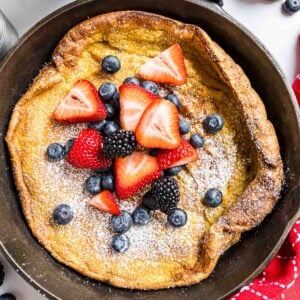 A German Pancake topped with powdered sugar and berries, baked in a cast iron skillet.