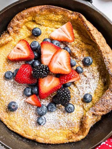 A German Pancake topped with powdered sugar and berries, baked in a cast iron skillet.