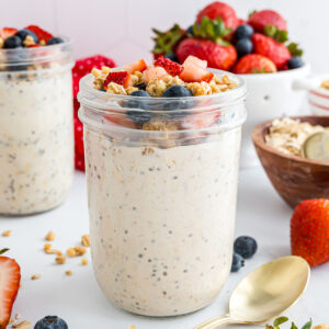 A jar of high-protein overnight oats topped with protein granola, blueberries, and strawberries.
