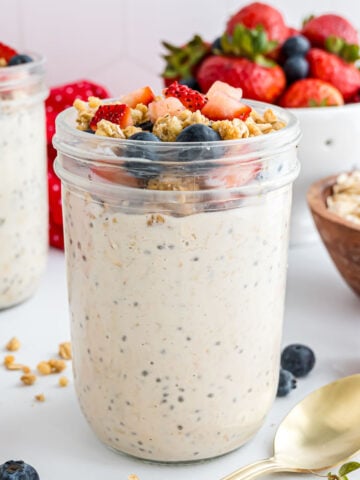 A jar of high-protein overnight oats topped with protein granola, blueberries, and strawberries.