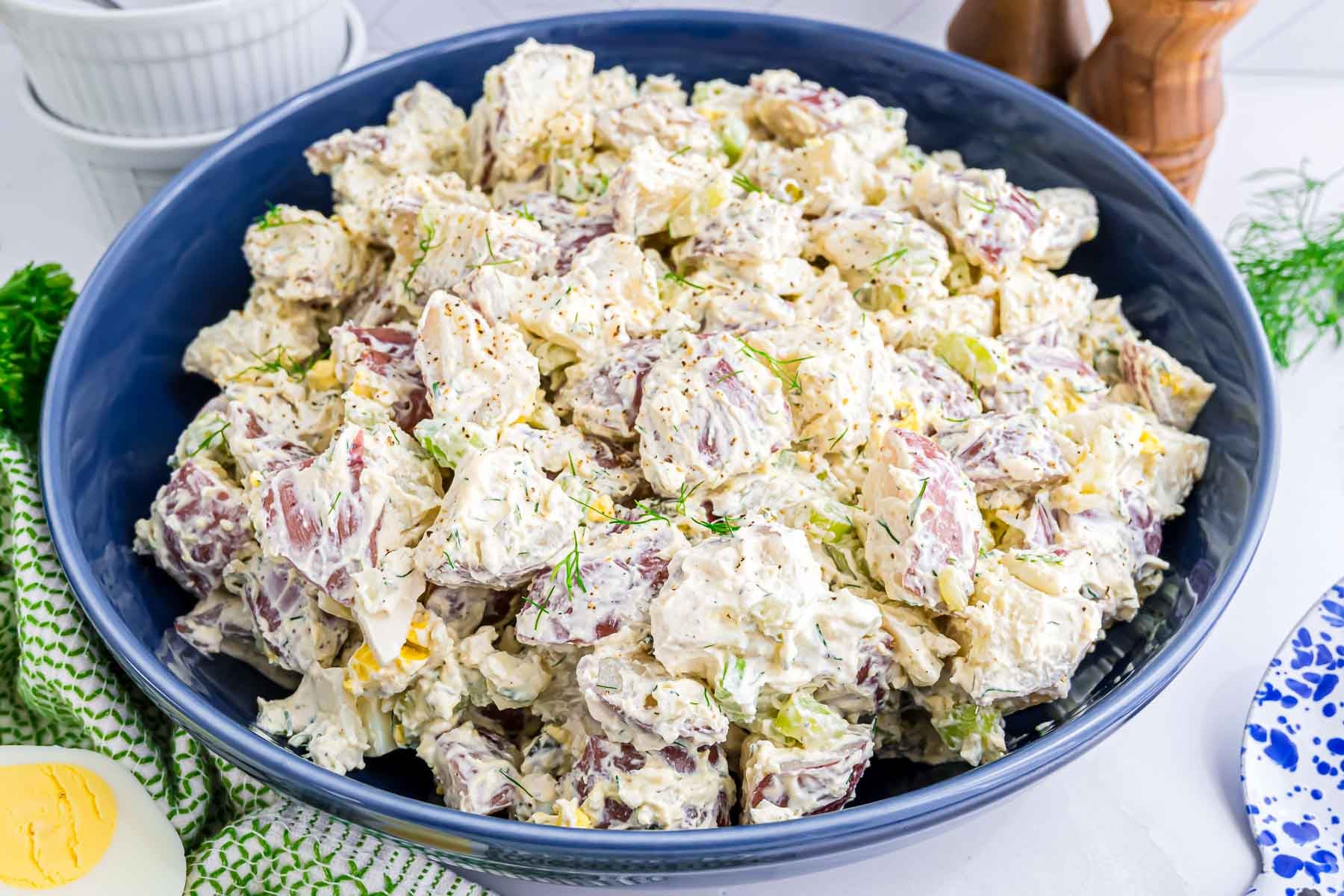 Red Potato Salad with a creamy dressing featuring hard boiled eggs, dill pickle, celery, onion, and fresh dill, in a large serving bowl.