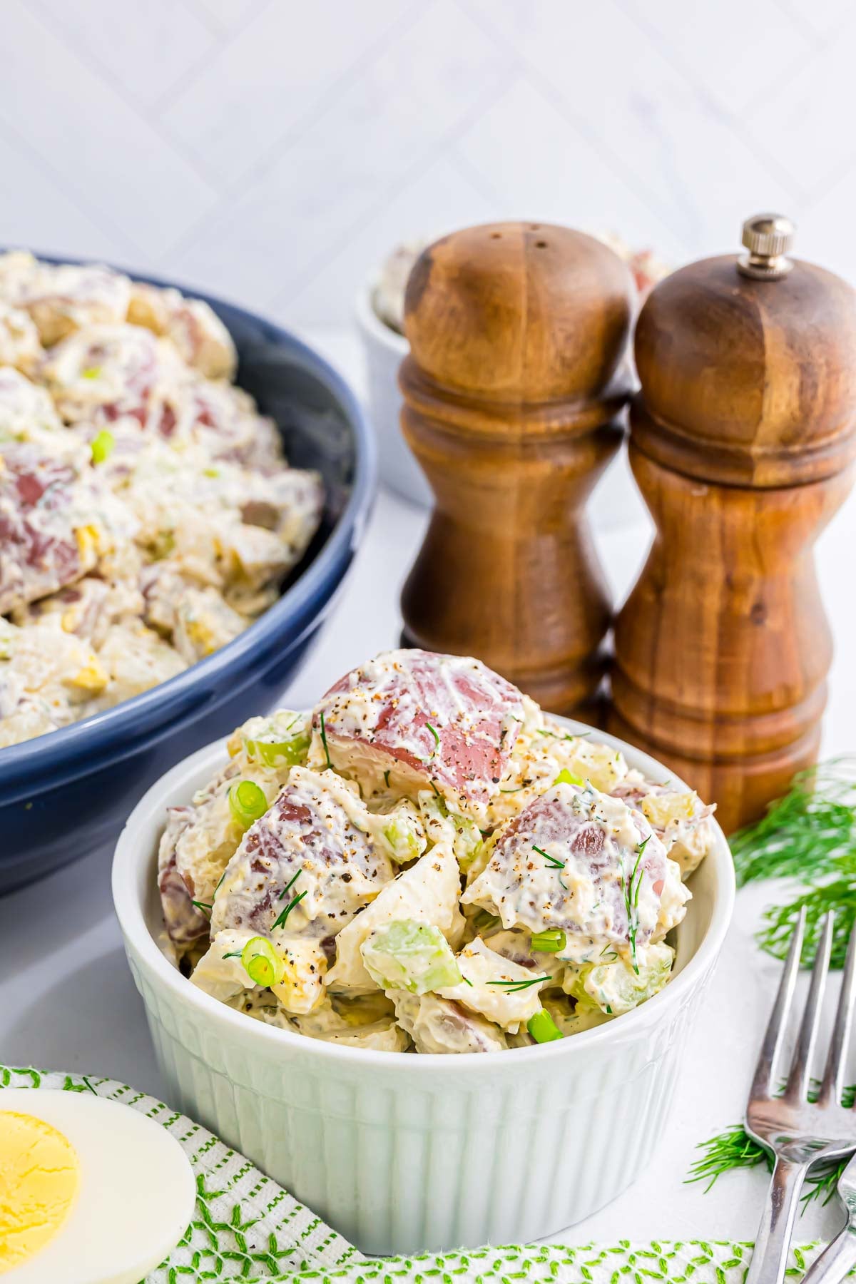 Red Potato Salad with a creamy dressing featuring hard boiled eggs, dill pickle, celery, onion, and fresh dill, in a small ramekin.