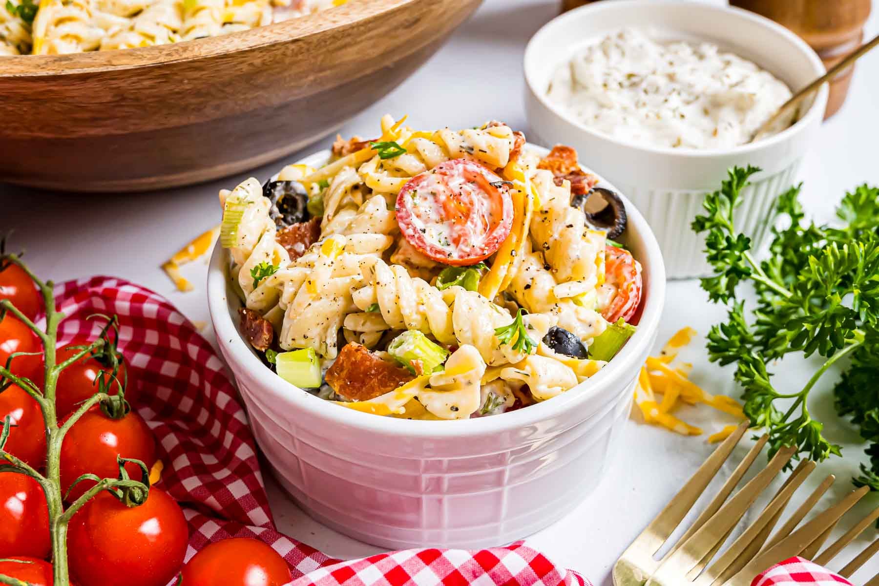 A small white ceramic ramekin filled with a scoop of creamy Bacon Ranch Pasta Salad, featuring visible rotini, crumbles of crispy bacon, and fresh herbs.