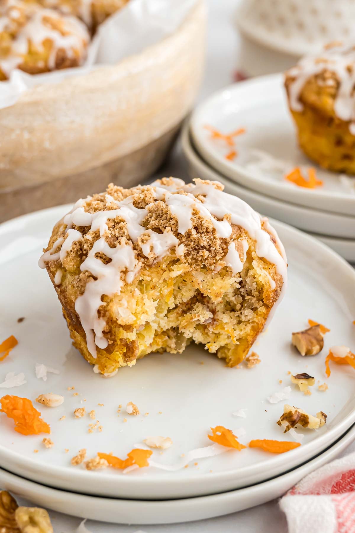 A morning glory muffin on a small serving plate with a bite taken out of it to reveal the inside texture, bits of coconut and shredded carrot.